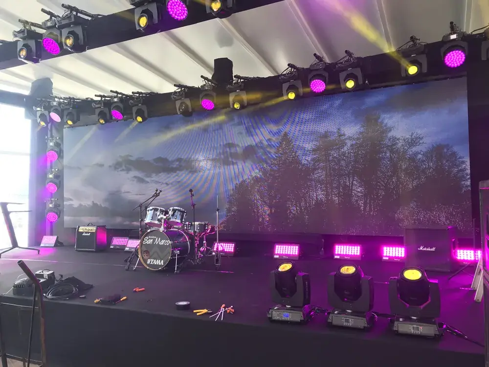Palco ao ar livre com iluminação roxa entre árvores